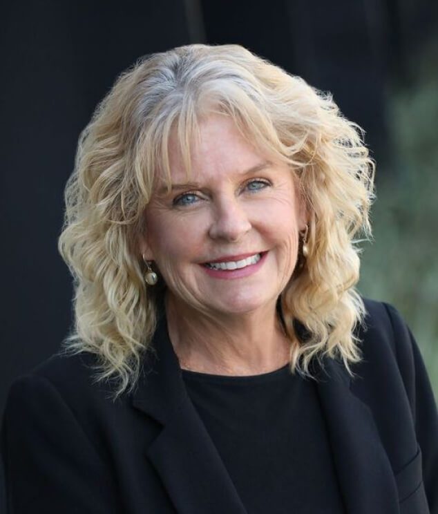 A woman with blonde hair and blue eyes wearing black.