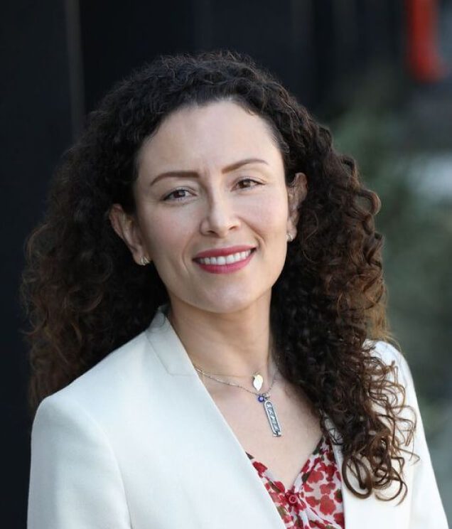 A woman with long curly hair wearing a white jacket.