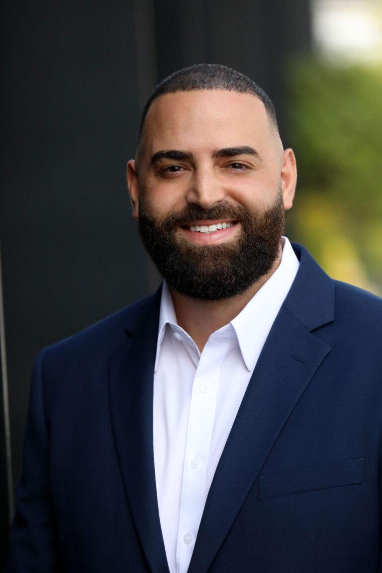 A man with beard and suit jacket smiling for the camera.